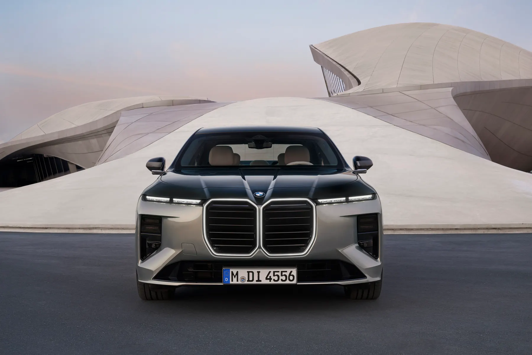 Grey 2027 BMW 740 xDrive, front three-quarter on a mountain road with Iconic Glow kidneys and slim upper lamps