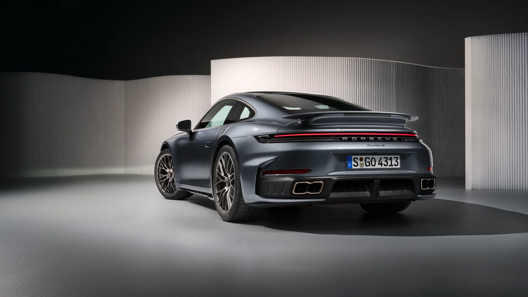 Gray 2026 Porsche 911 Turbo S coupe, front three-quarter with tinted headlamps and the four-point graphic lit