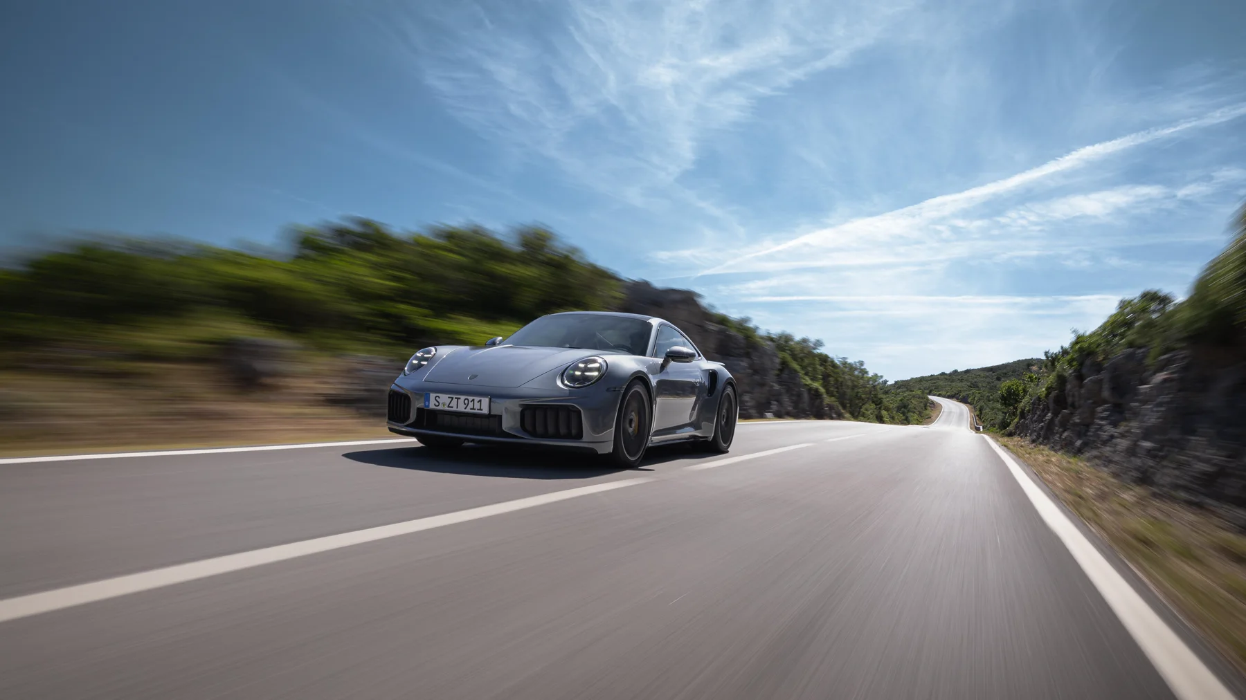 Gray 2026 Porsche 911 Turbo S, rear three-quarter with a full-width taillight bar and Porsche lettering