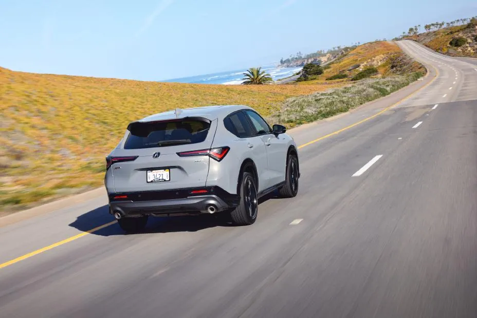 Gray 2026 Acura ADX A-Spec, rear three-quarter on a mountain road with wide-set LED taillights and dual exhaust finishers