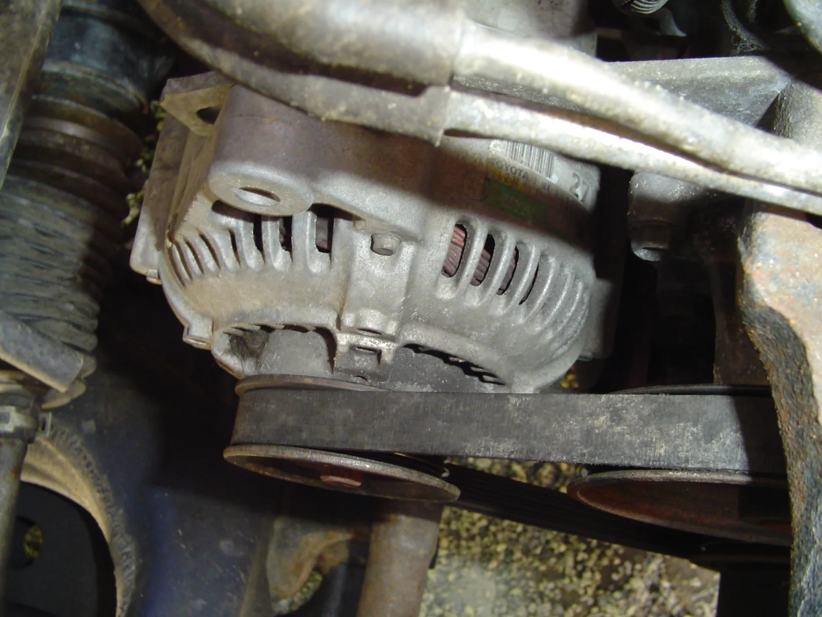 Toyota Corolla alternator in the bay, serpentine belt on the pulley and stator visible through the vents