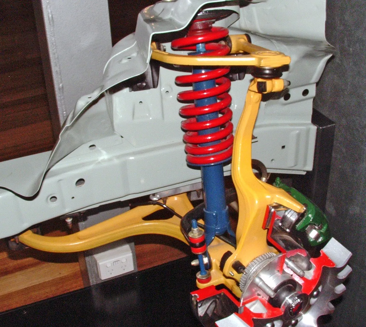 Double-wishbone corner with the upper and lower control arms and upright painted yellow, coil and damper in red and blue