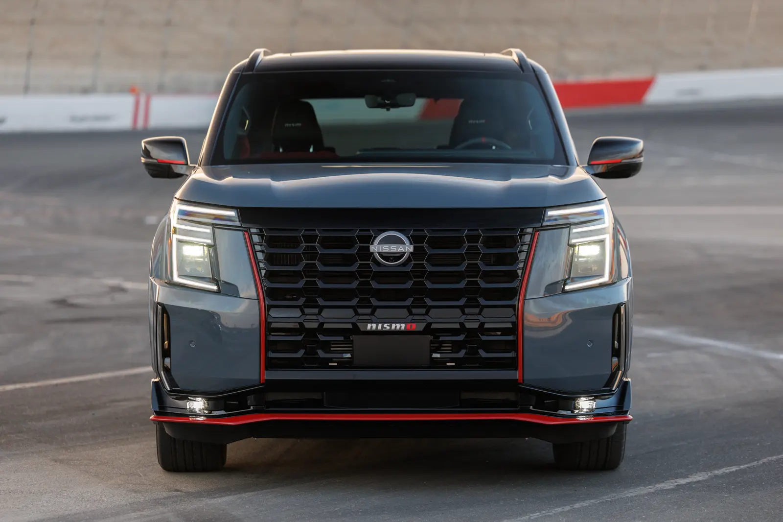Stealth Gray 2026 Nissan Armada NISMO, dead-front on a racetrack with hex V-motion mesh and a nismo grille stamp