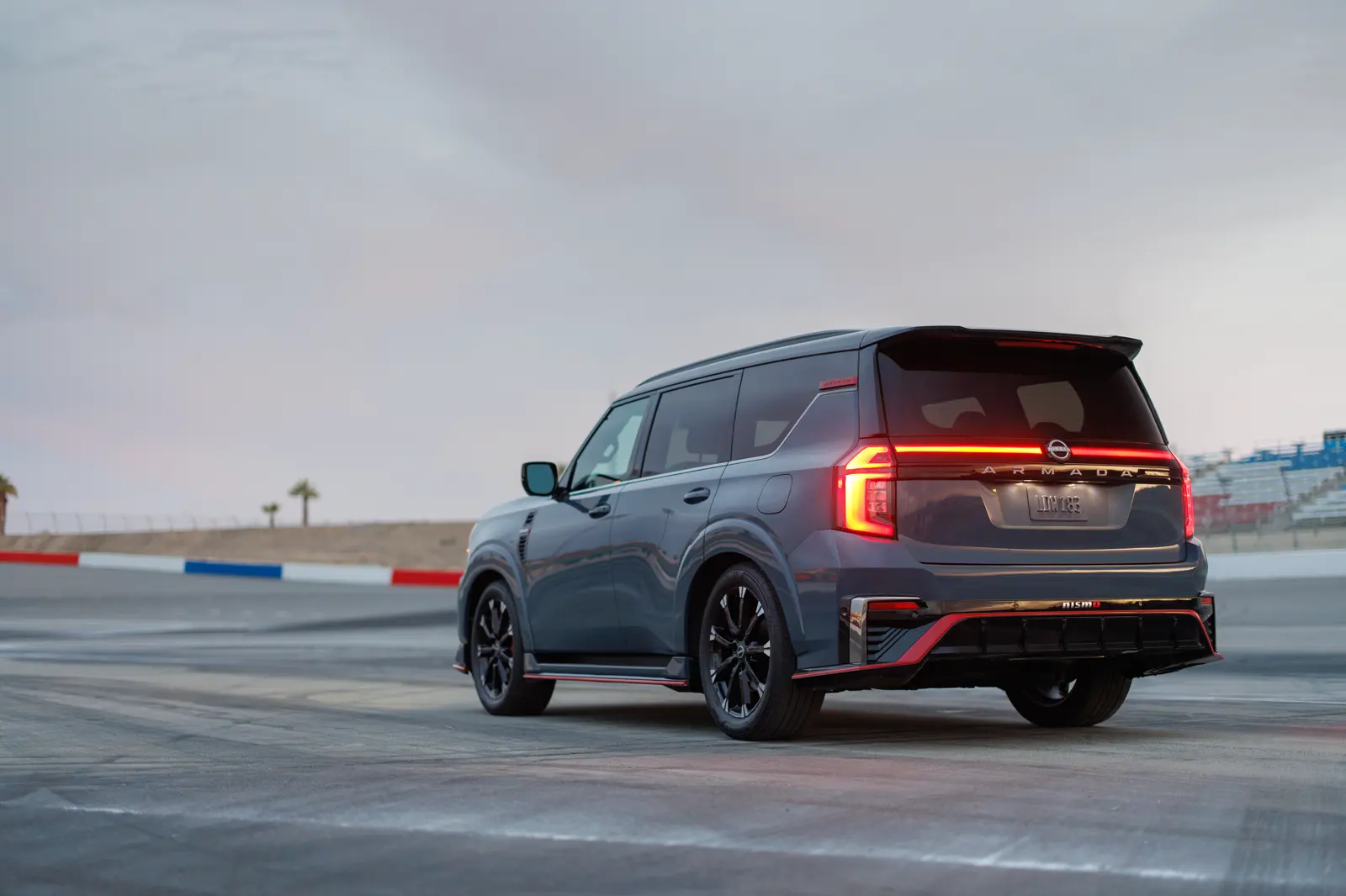 Stealth Gray 2026 Nissan Armada NISMO, rear three-quarter on a racetrack with ARMADA in a lit bar