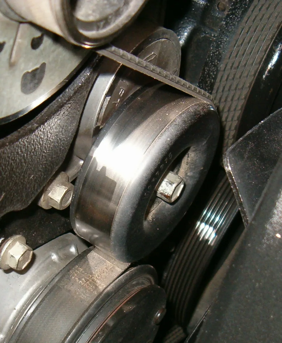 Smooth idler pulley riding the flat back of a serpentine belt, hex bolt in the hub