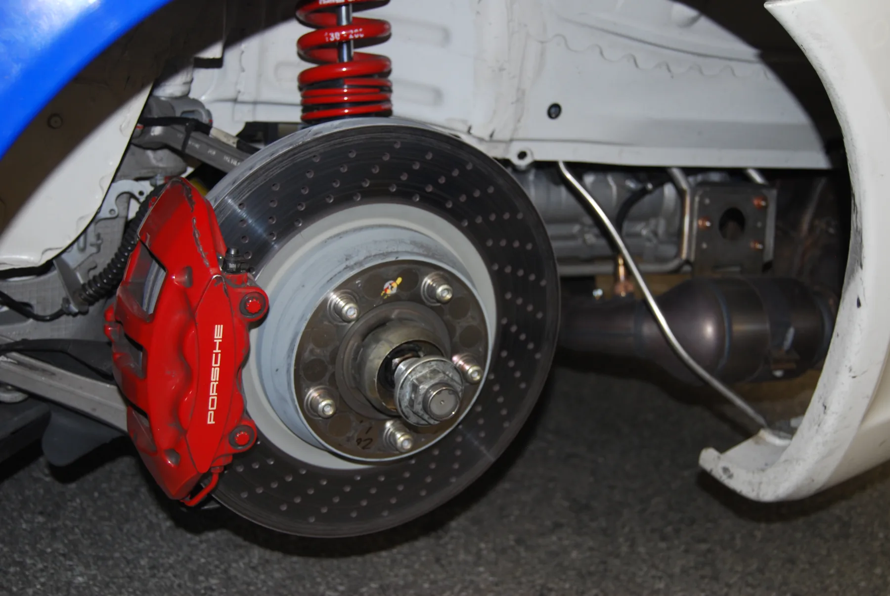 Red Porsche four-piston brake caliper clamped on a cross-drilled disc, wheel off