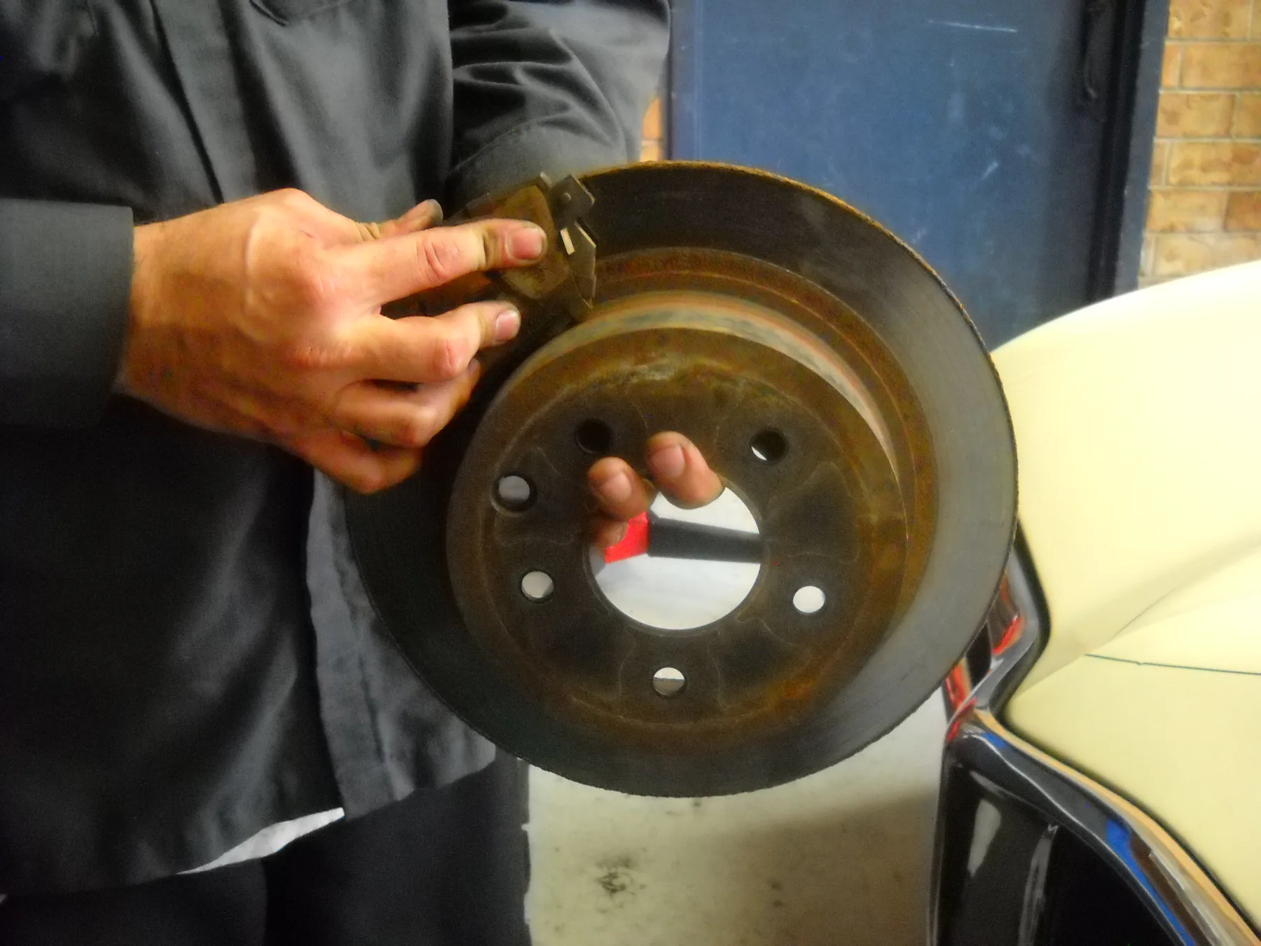 Hands holding a worn brake pad against a rusted disc rotor
