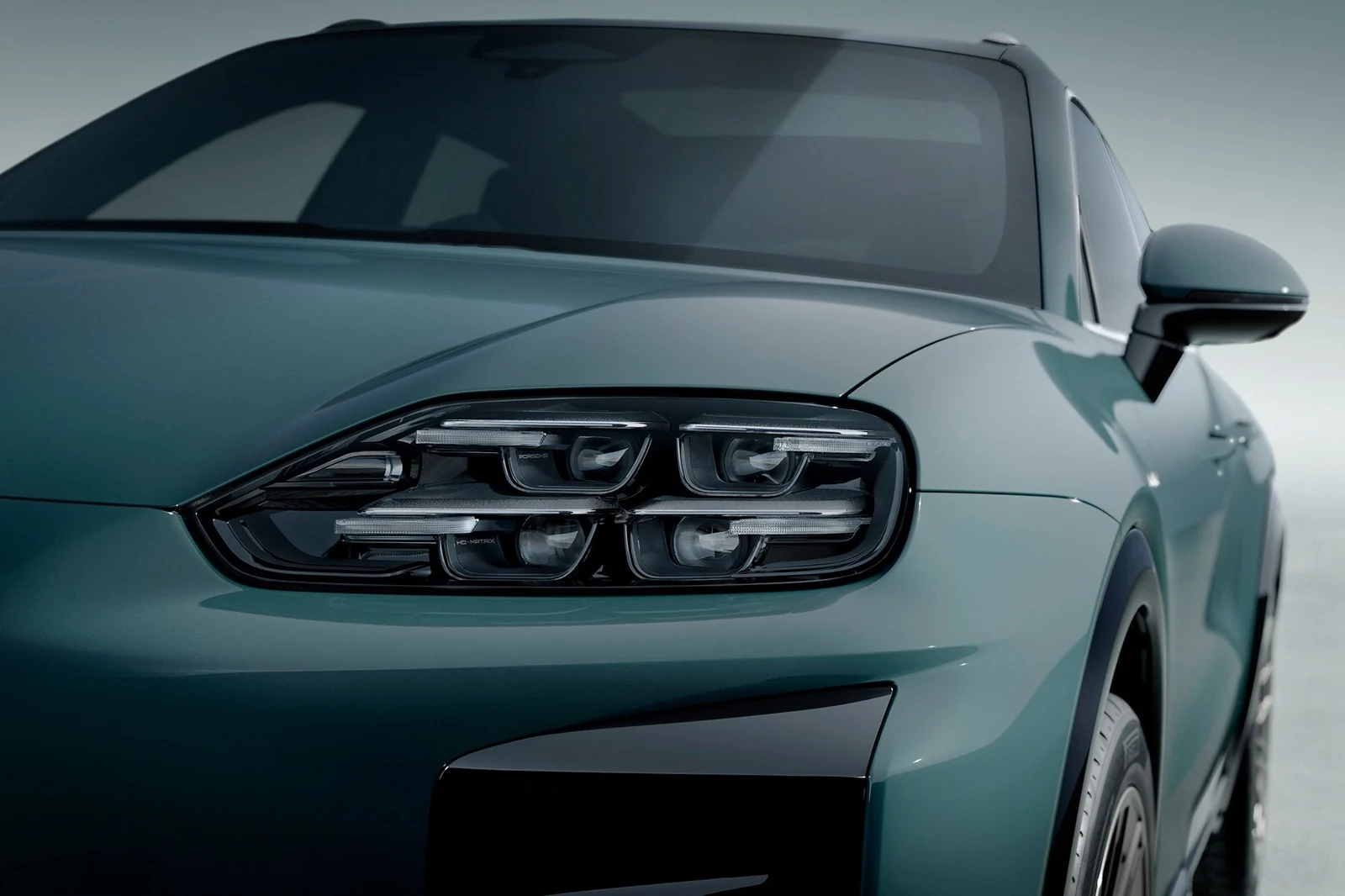 Mystic-green 2026 Porsche Cayenne Turbo Electric, studio close-up of a slim Matrix LED headlamp in a low hood