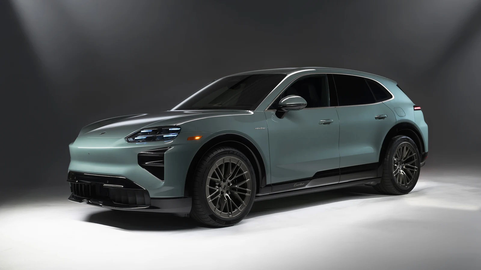 Mystic-green 2026 Porsche Cayenne Turbo Electric, studio front three-quarter with slim Matrix LED lamps lit