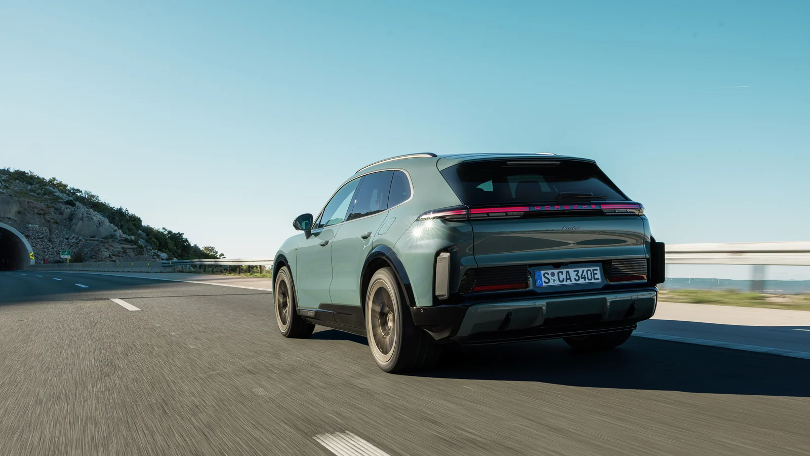 Mystic-green 2026 Porsche Cayenne Turbo Electric, rear three-quarter on a coastal road with a full-width light strip