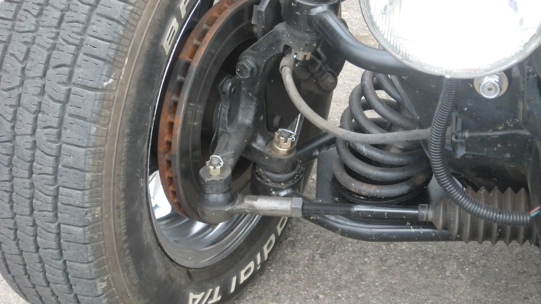 Front suspension of a 1932 Ford: coil spring in a perch between the frame and the axle, a separate shock absorber beside the spring, and a disc brake at the hub