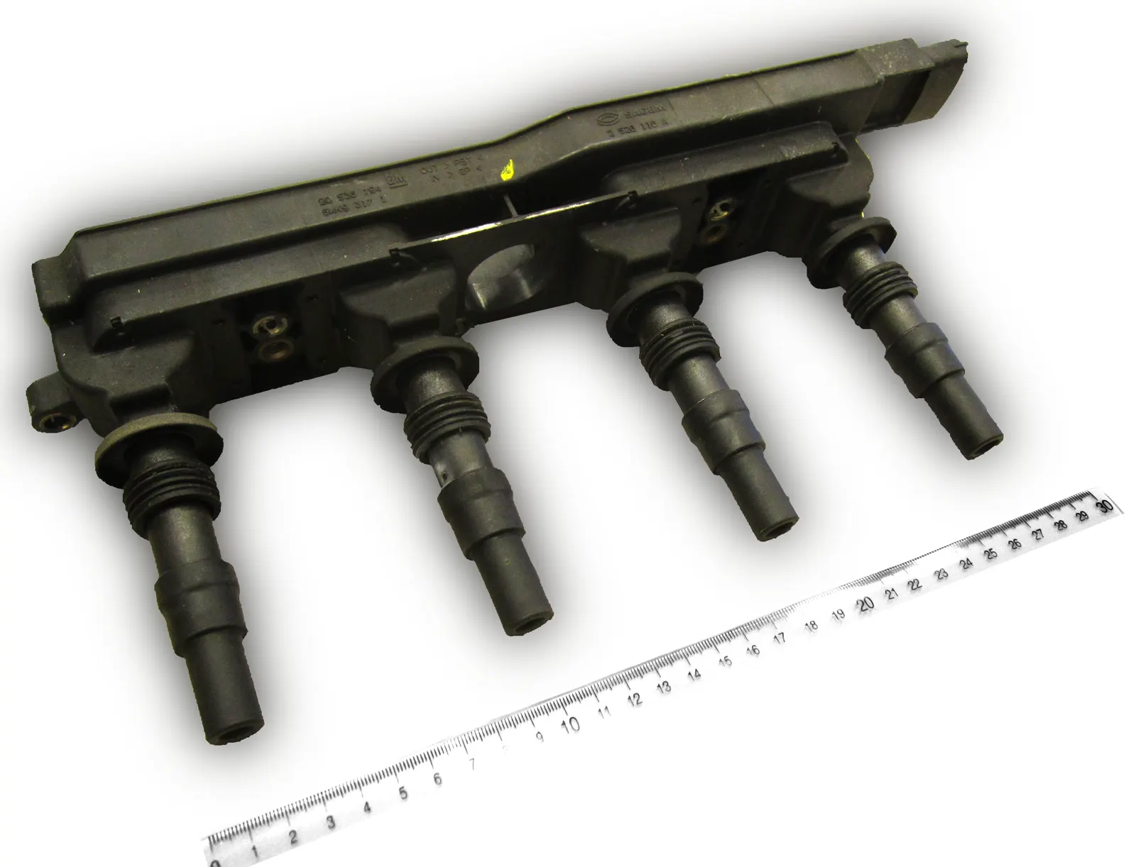 Four-well ignition coil module with boots and a wiring connector, ruler for scale