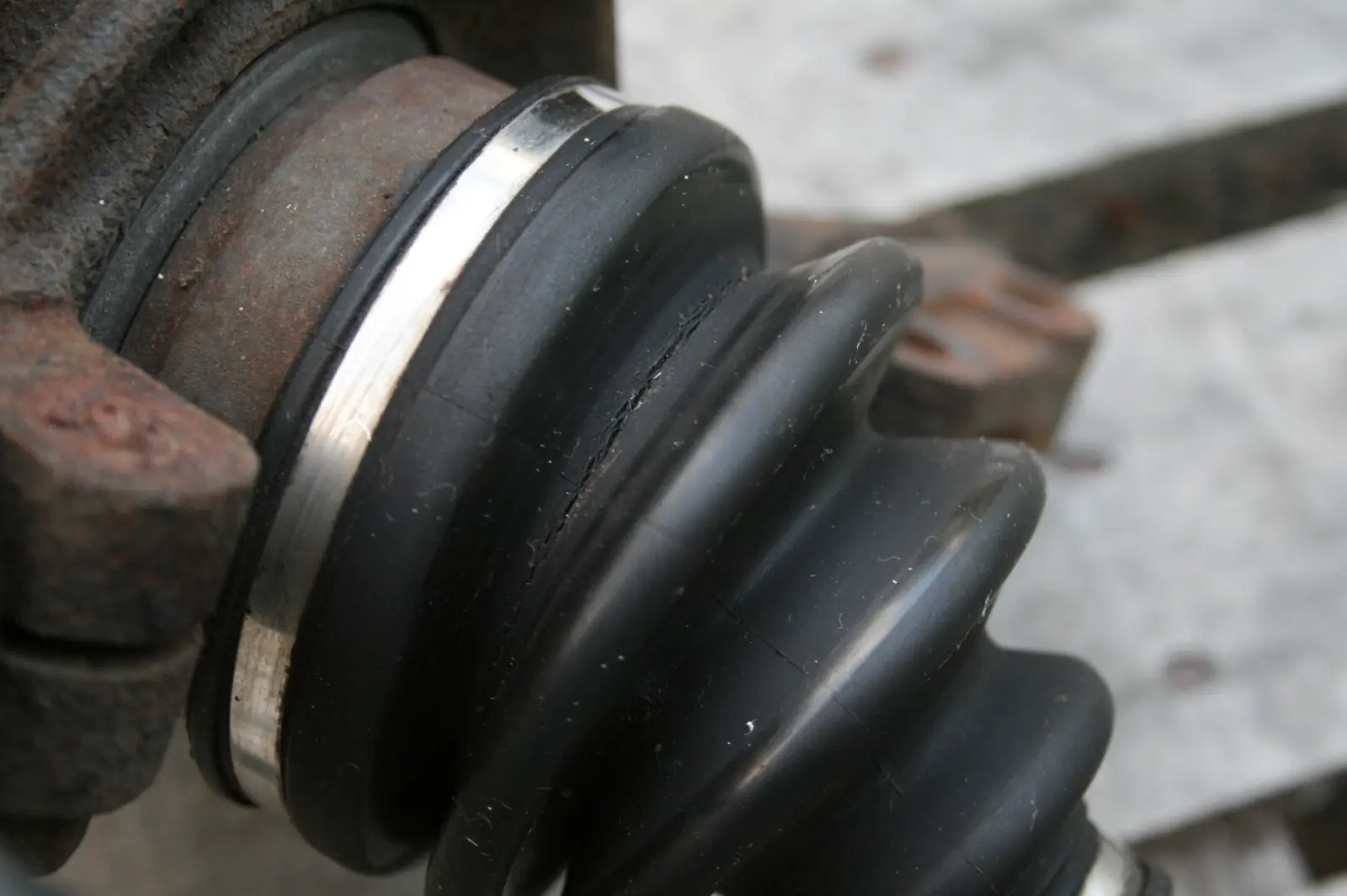 Close-up of a cracked CV boot, ribbed rubber and a metal clamp on the joint housing