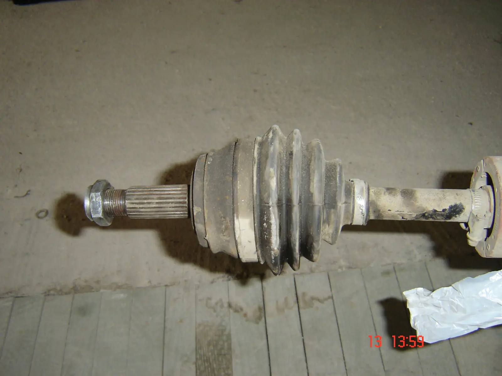 Front half-shaft on a floor, outer CV joint in a ribbed rubber boot, splined stub and axle nut