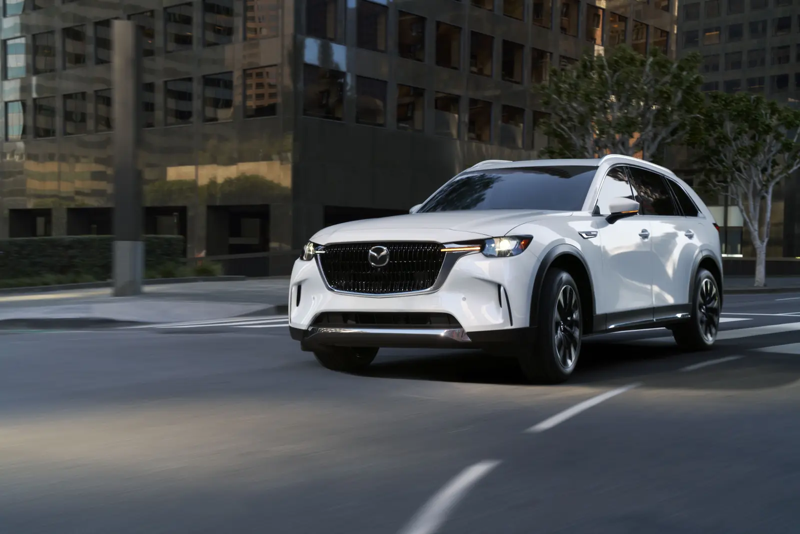 White 2026 Mazda CX-90, front three-quarter rolling in a city corridor with a chrome Signature Wing across the black mesh grille