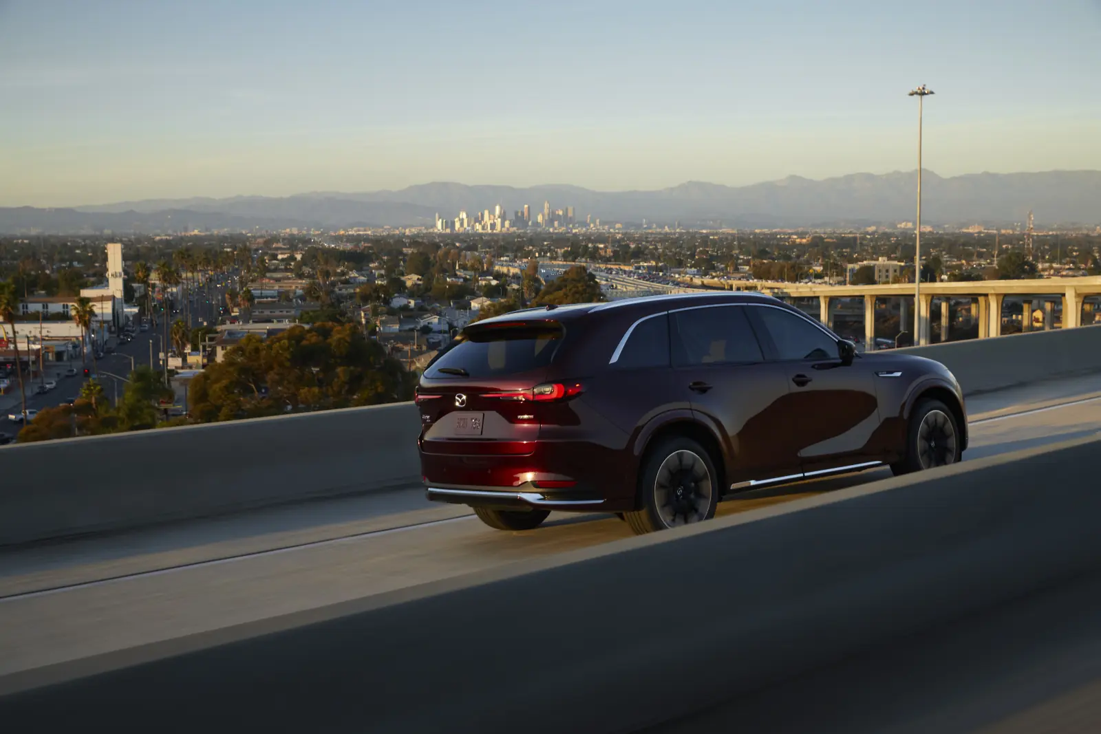 Soul Red 2026 Mazda CX-90, rear three-quarter on an elevated highway with slim tail lamps