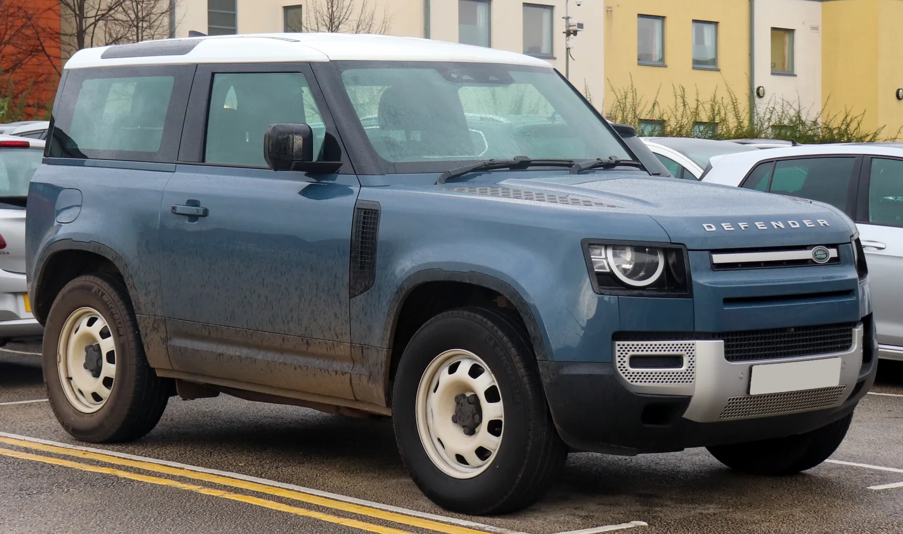 Front three-quarter of a blue 2022 Land Rover Defender 90 with a white roof, steel wheels, DEFENDER lettering on the hood edge, and a round lamp inside a squared housing