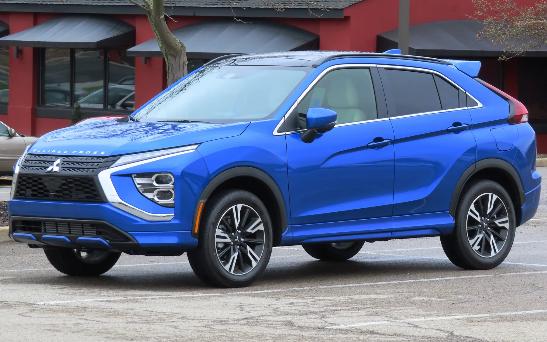 Front three-quarter of a blue 2023 Mitsubishi Eclipse Cross SEL Touring with a dark grille, a thin lamp at the leading edge of the hood, a lower lamp in the bumper, and Eclipse Cross lettering on the hood