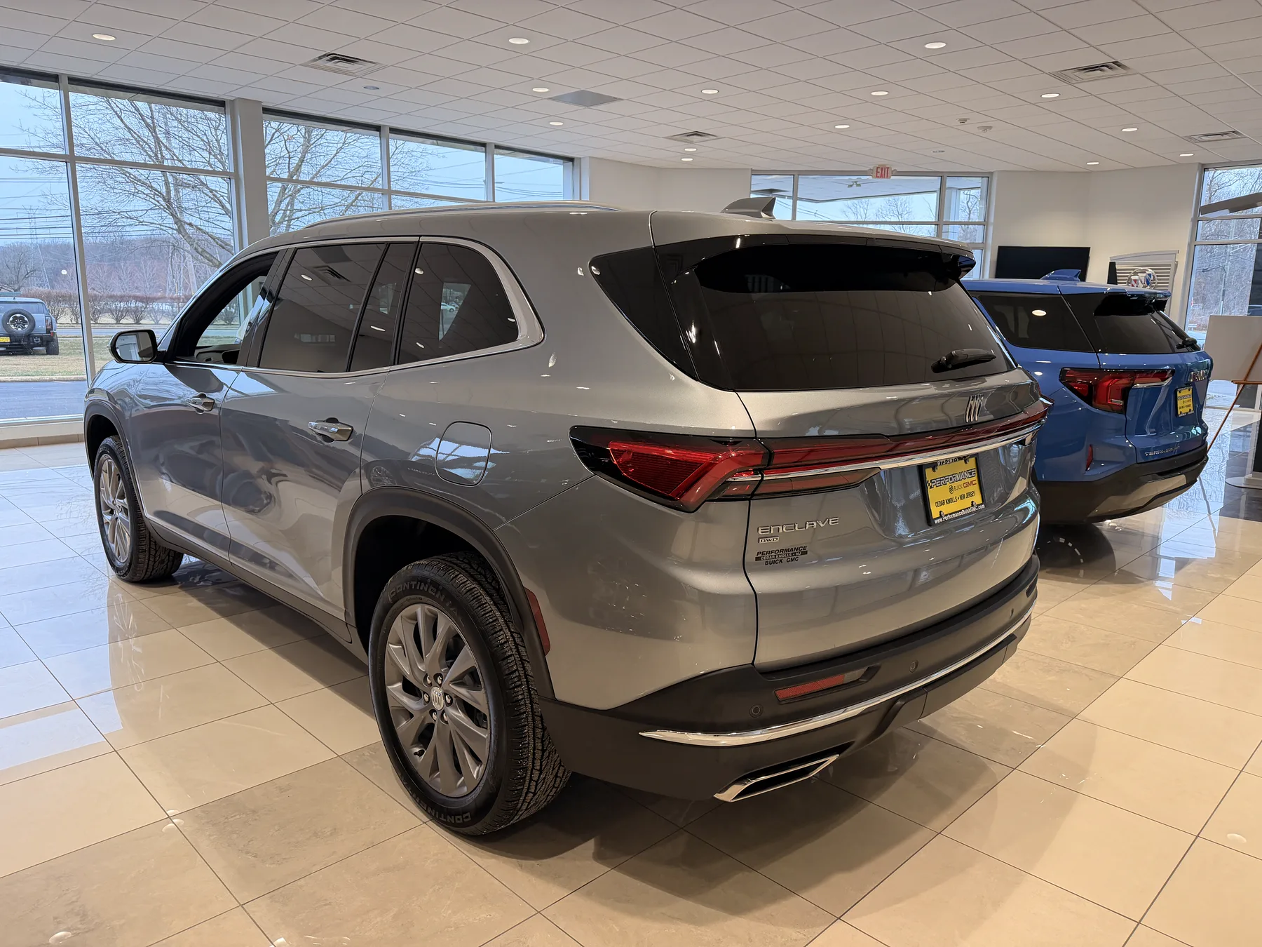 Rear three-quarter of a 2026 Buick Enclave in a showroom, with a wide LED taillamp across the tailgate