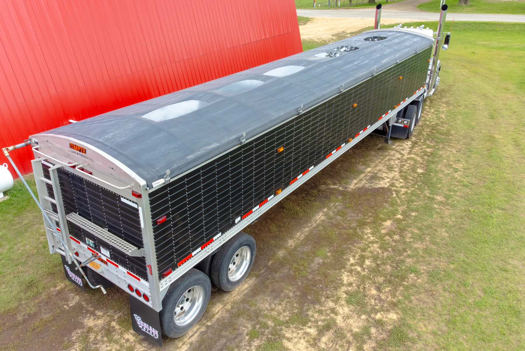 Empty Timpte grain hopper trailer parked on gravel, with no license plate on the rear
