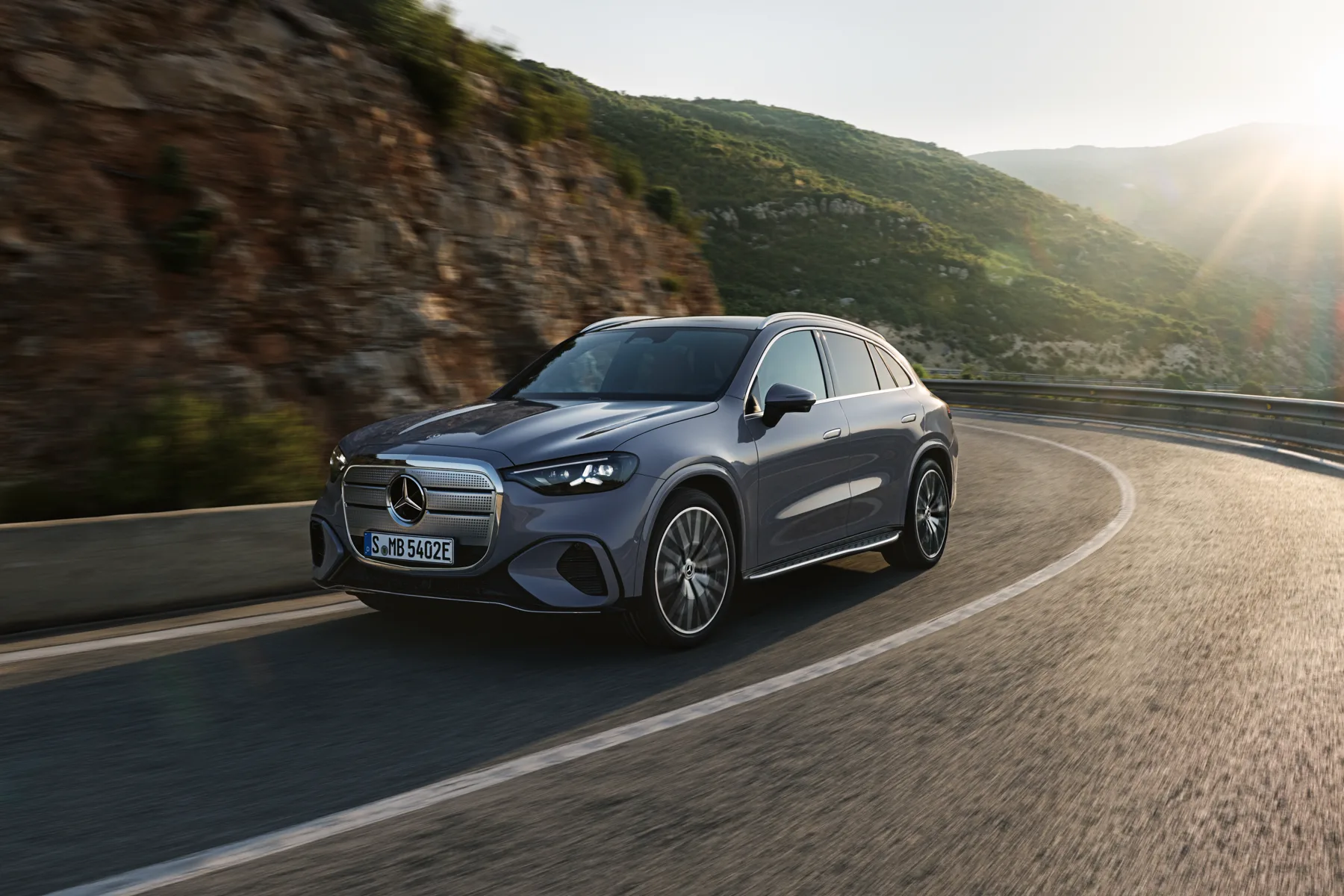 Sky blue 2027 Mercedes-Benz GLC 400 4MATIC Electric, front three-quarter on a coastal road with an illuminated chrome grille, European model shown