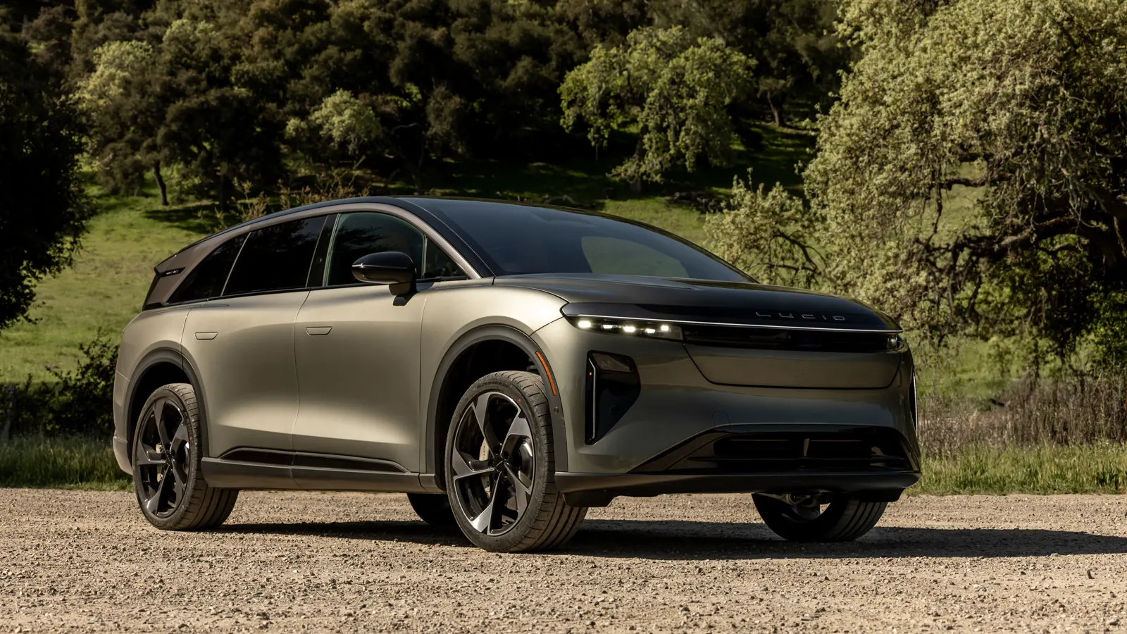 Bronze 2026 Lucid Gravity Grand Touring, front three-quarter on a gravel road with blade DRL lamps and a glass canopy