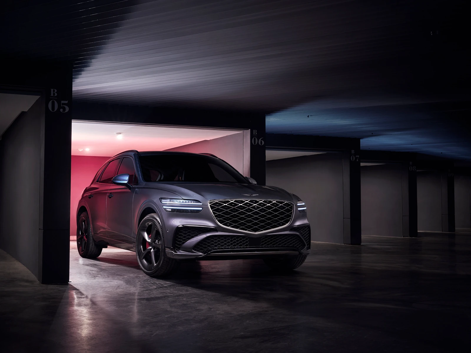 Charcoal 2026 Genesis GV70 Sport, front three-quarter in a garage with two-line lamps and a dual-weave crest grille