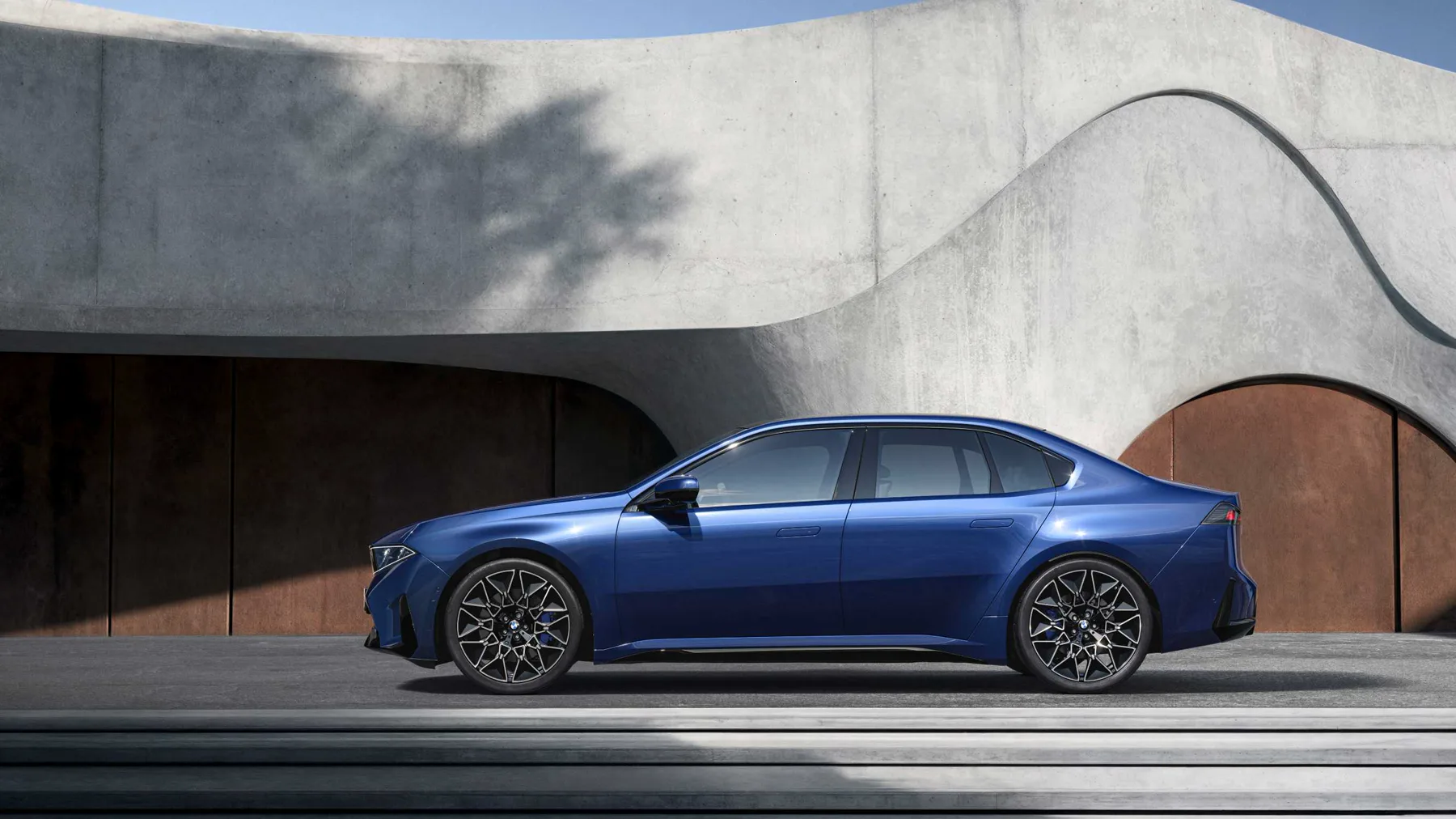 Blue 2026 BMW i3 50 xDrive in side profile against a concrete wall