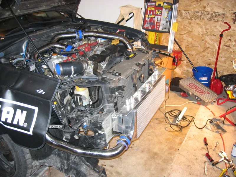 Front-mount intercooler core being fitted in the nose of a Subaru WRX STI, with end tanks and open charge pipes in the bumper opening