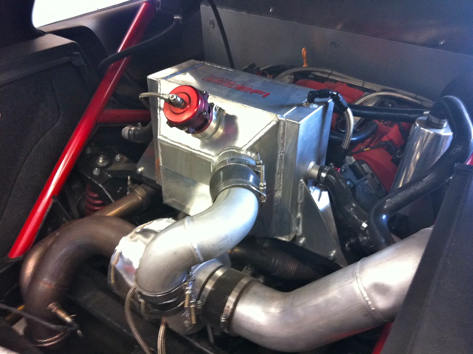 Air-to-liquid intercooler core with coolant hoses, mounted beside a large turbocharger in a mid-engine bay