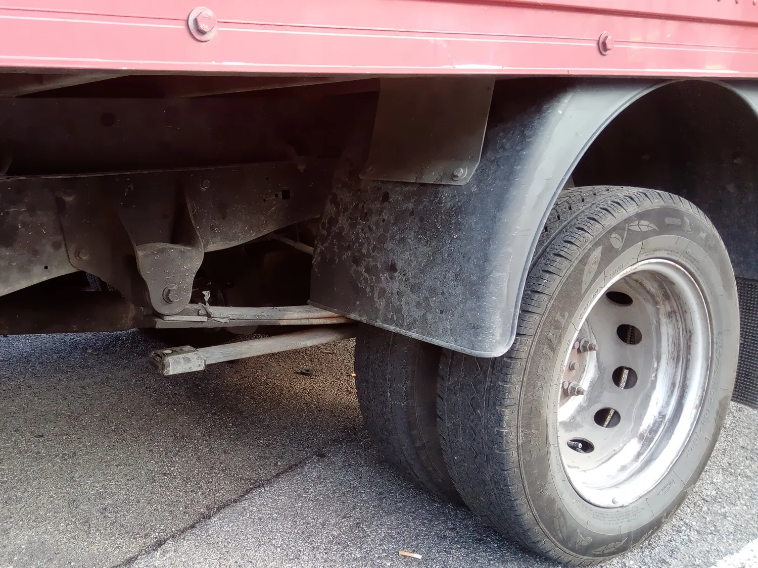 Leaf spring off the vehicle on gravel, with a full-length leaf ending in an eye at each end and shorter leaves stacked beneath it