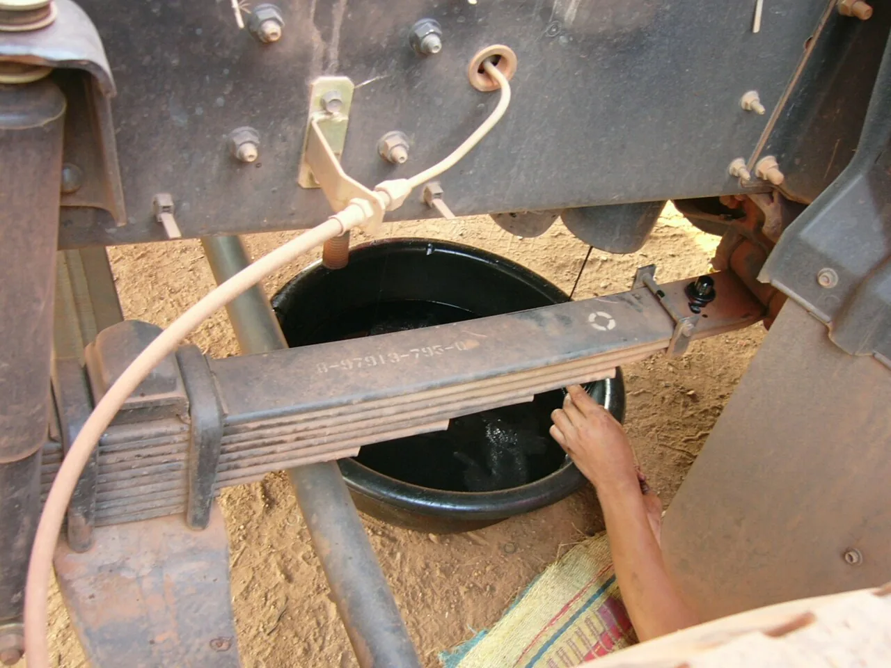 Underside of a truck with a stack of leaf springs clamped to the axle by U-bolts and an oil drain plug on the housing above the pack