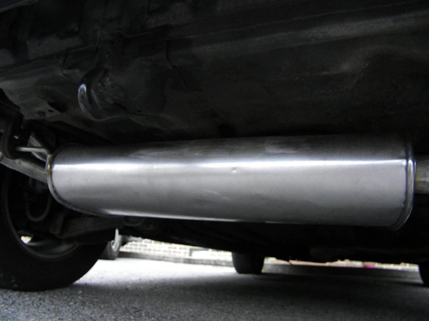 Cylindrical metal muffler installed beneath a vehicle