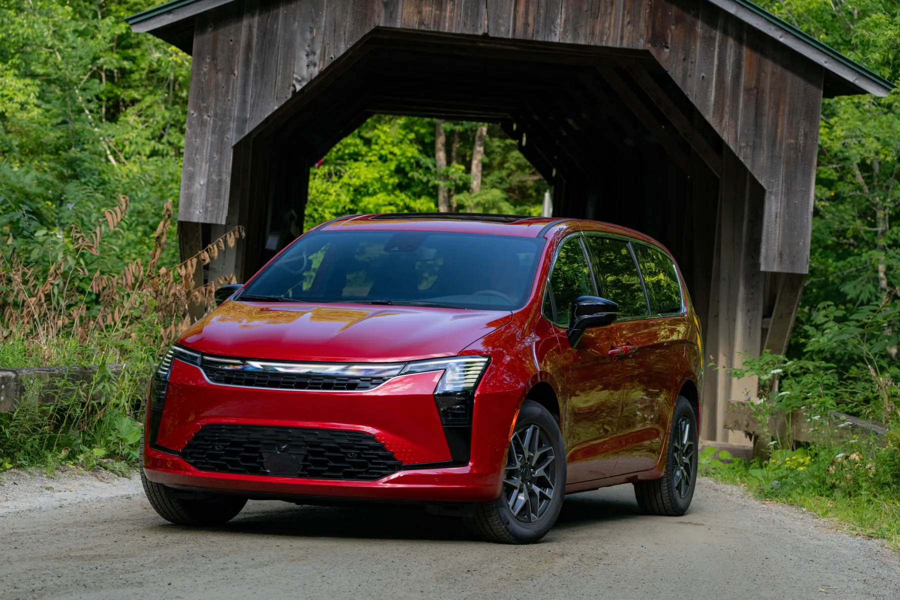 Red 2027 Chrysler Pacifica Limited, front three-quarter in a studio with piano-key lamps and an illuminated wing badge