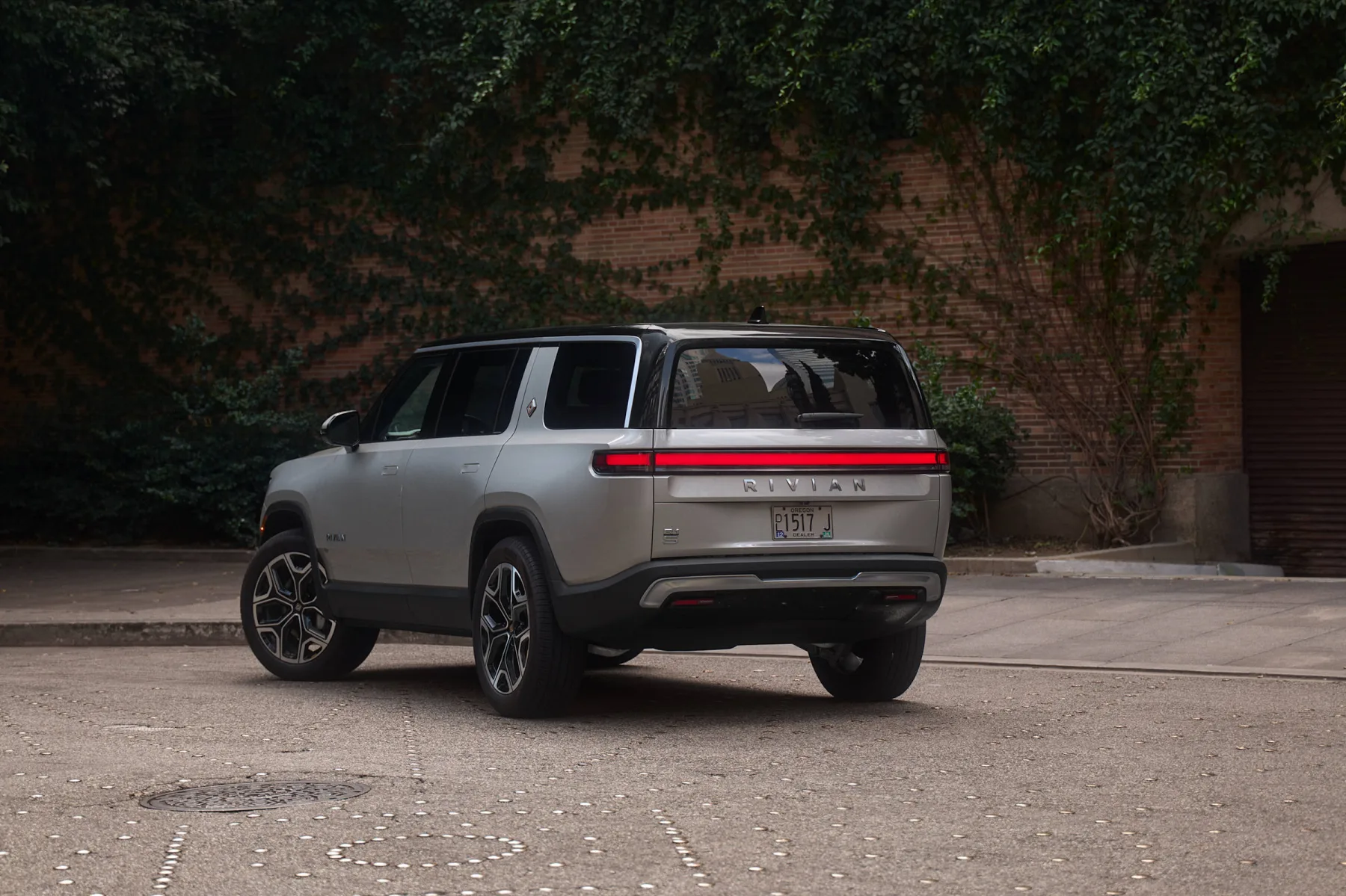 Silver 2026 Rivian R1S, rear three-quarter with a full-width red light bar and boxed greenhouse
