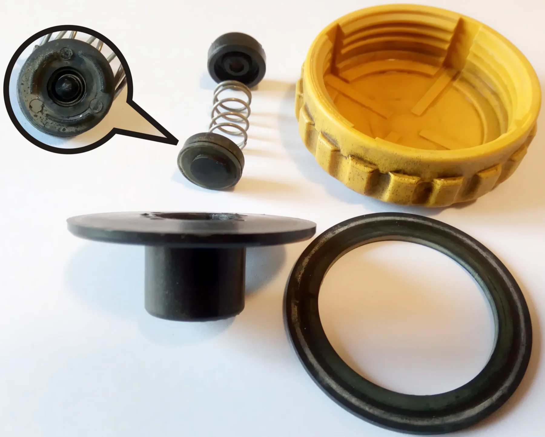 Disassembled radiator pressure cap: yellow shell, coil spring, rubber seat, and valve