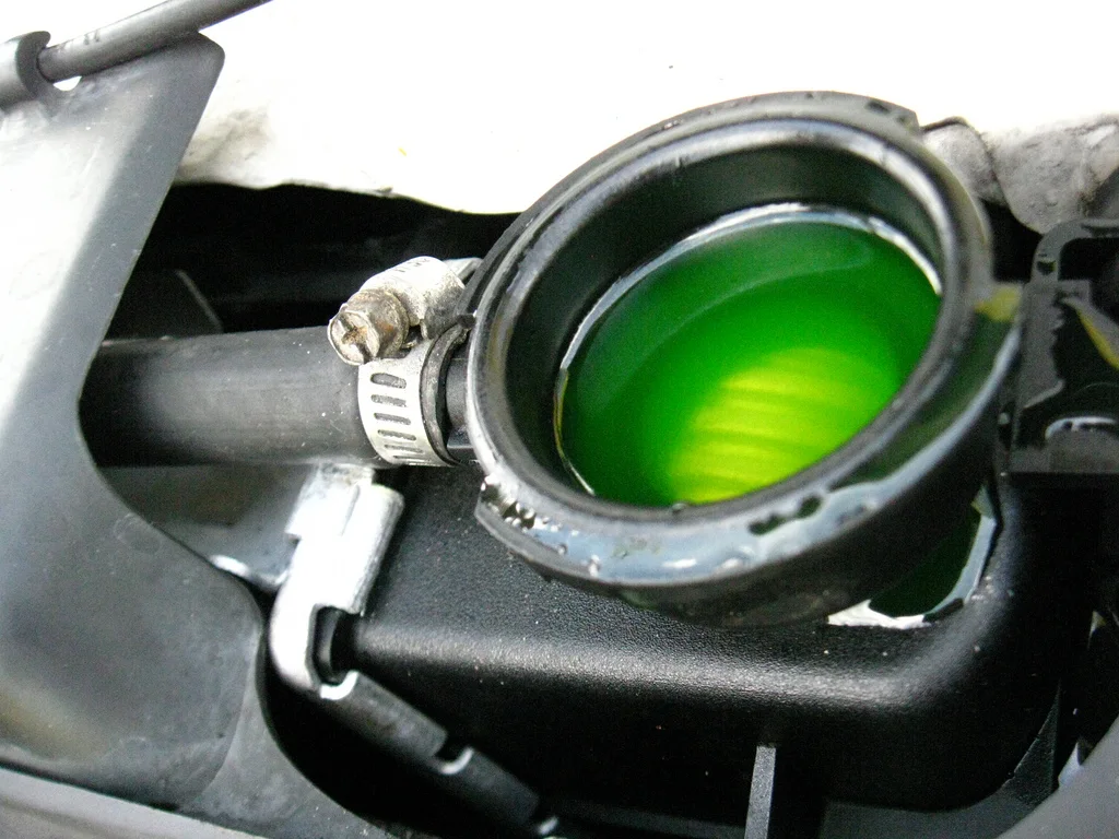 Open radiator neck filled with green coolant, hose and clamp on the side