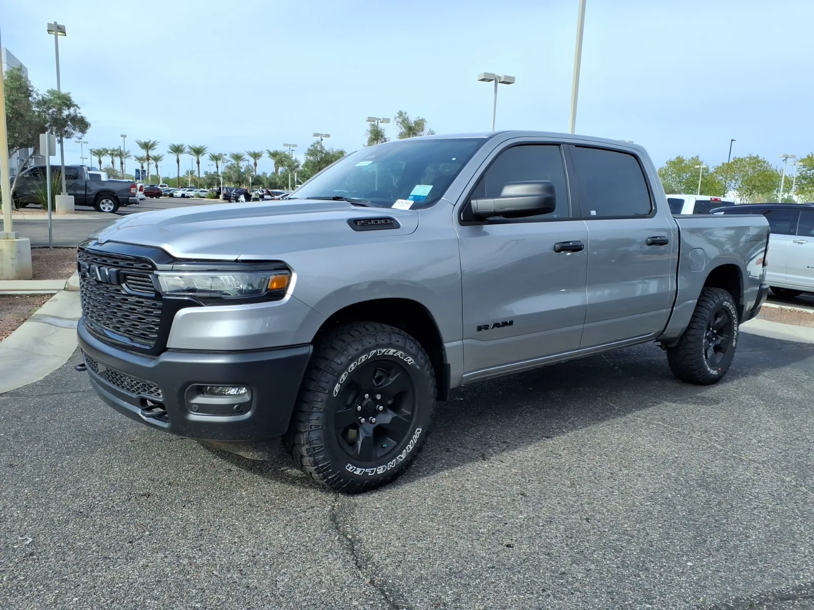 Front three-quarter of a 2026 Ram 1500 Warlock on a dealer lot, black grille with black RAM letters and red tow hooks