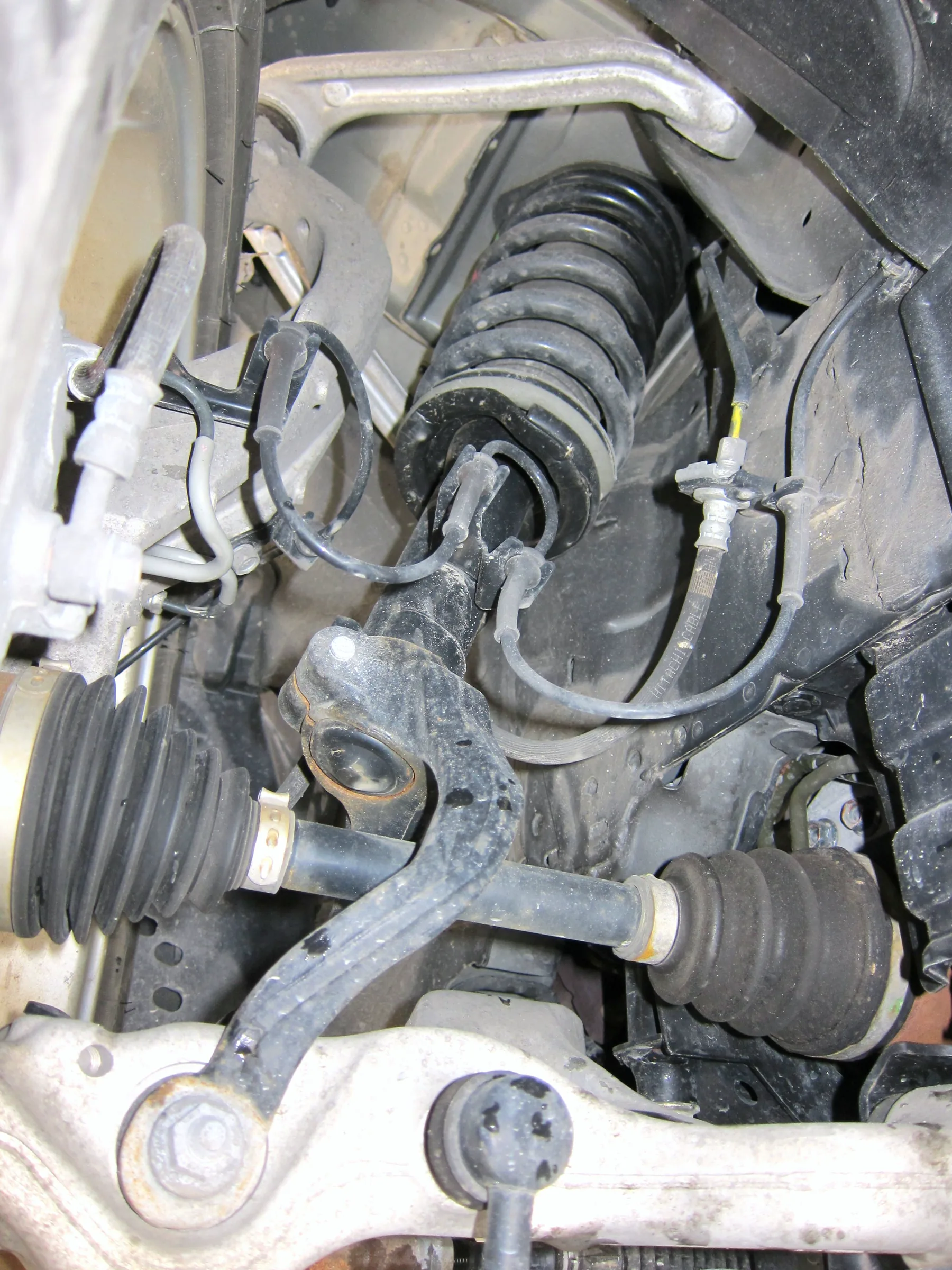 Right front corner of a 2008 Nissan Fuga with the wheel removed: coil spring wrapped around the shock absorber, brake disc and caliper beside the spring