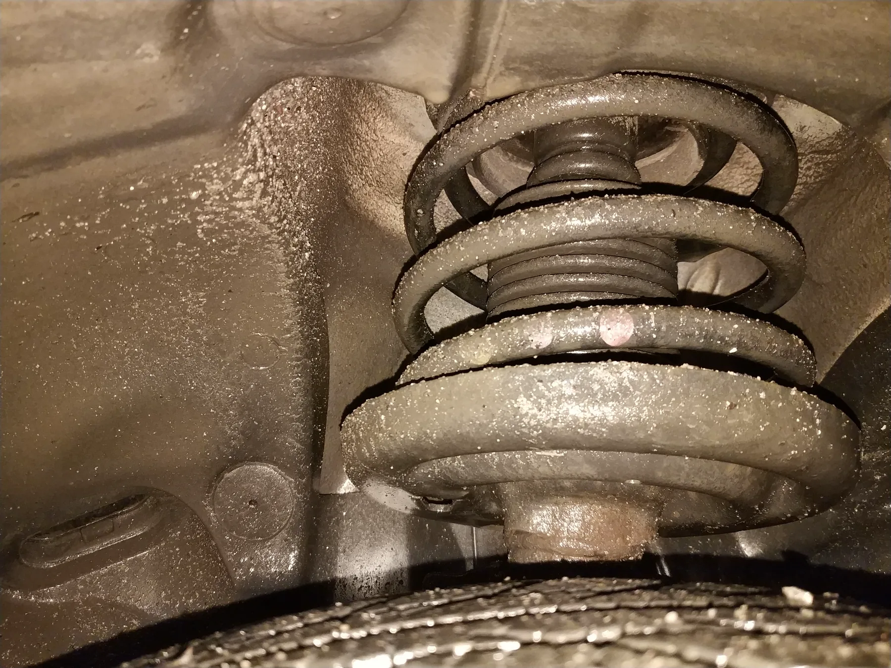 Shock absorber off the car with the coil spring still around the damper tube and an eye mount at each end, on a workshop floor