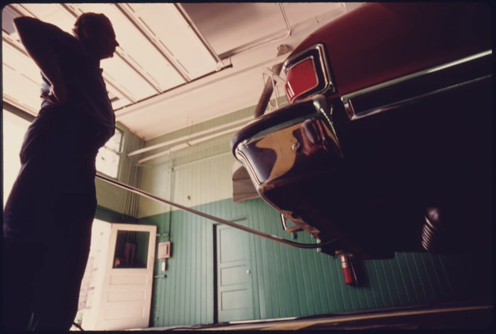 Inspector waits while a tailpipe probe runs from a red car at a U.S. emissions inspection station