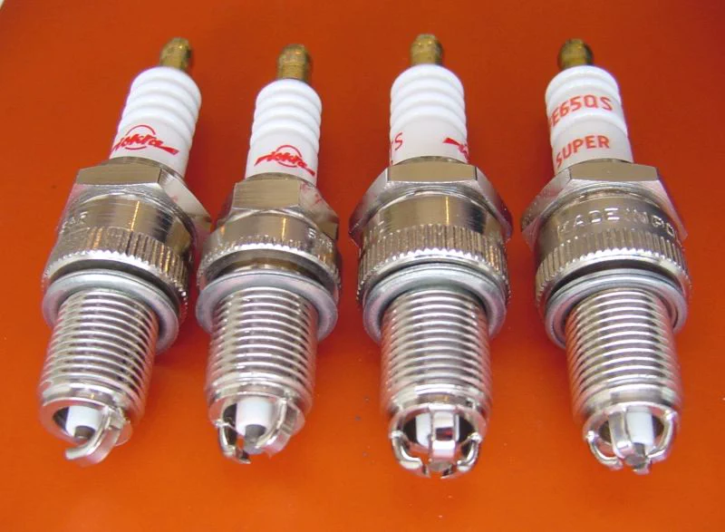 Four spark plugs on an orange field, ceramic insulators, hex shells, and J-gap ground electrodes