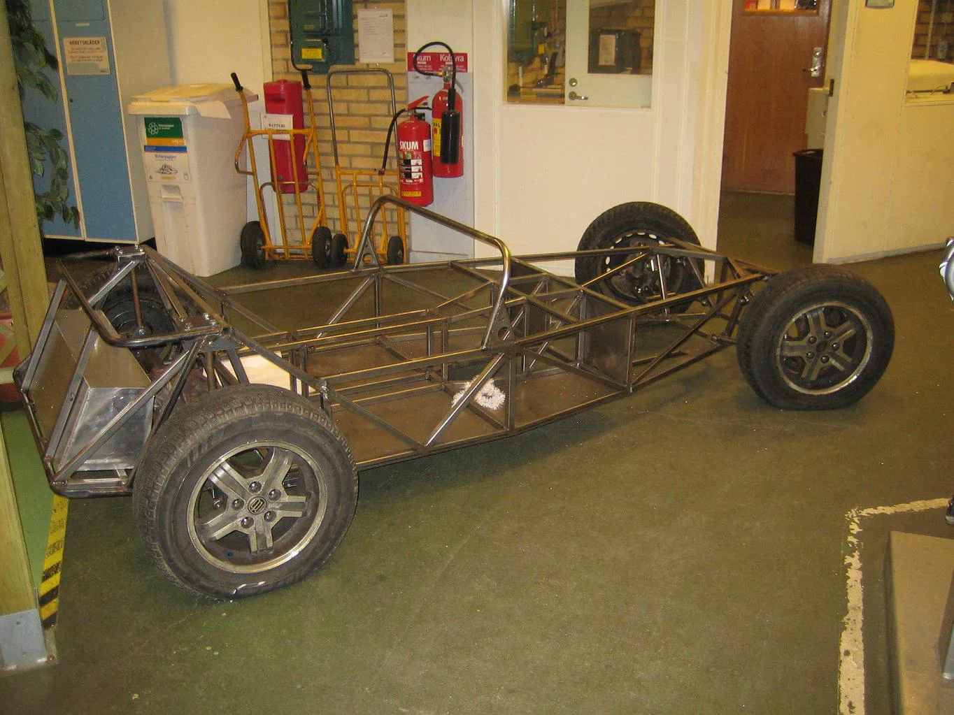 Bare steel tube spaceframe on four wheels and tires, indoors, with no body
