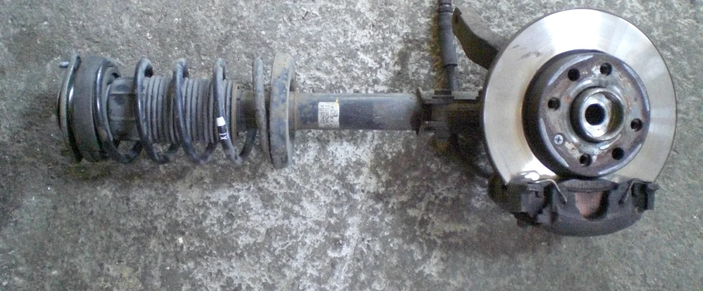 MacPherson strut assembly on concrete: coil and damper in one tube, knuckle, hub, disc, and caliper still attached