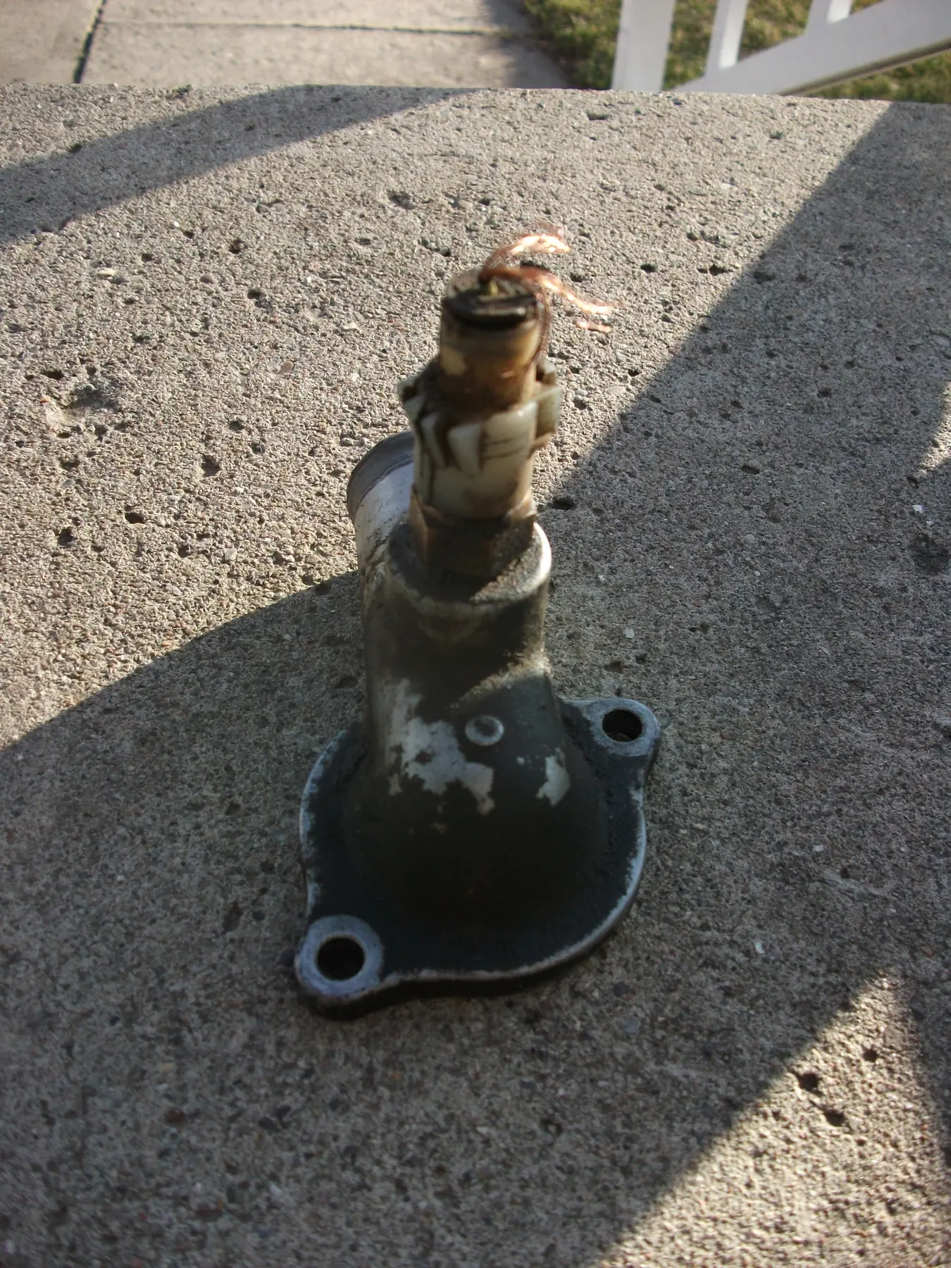 Cast thermostat housing on concrete with a frayed coolant-temperature switch in the neck