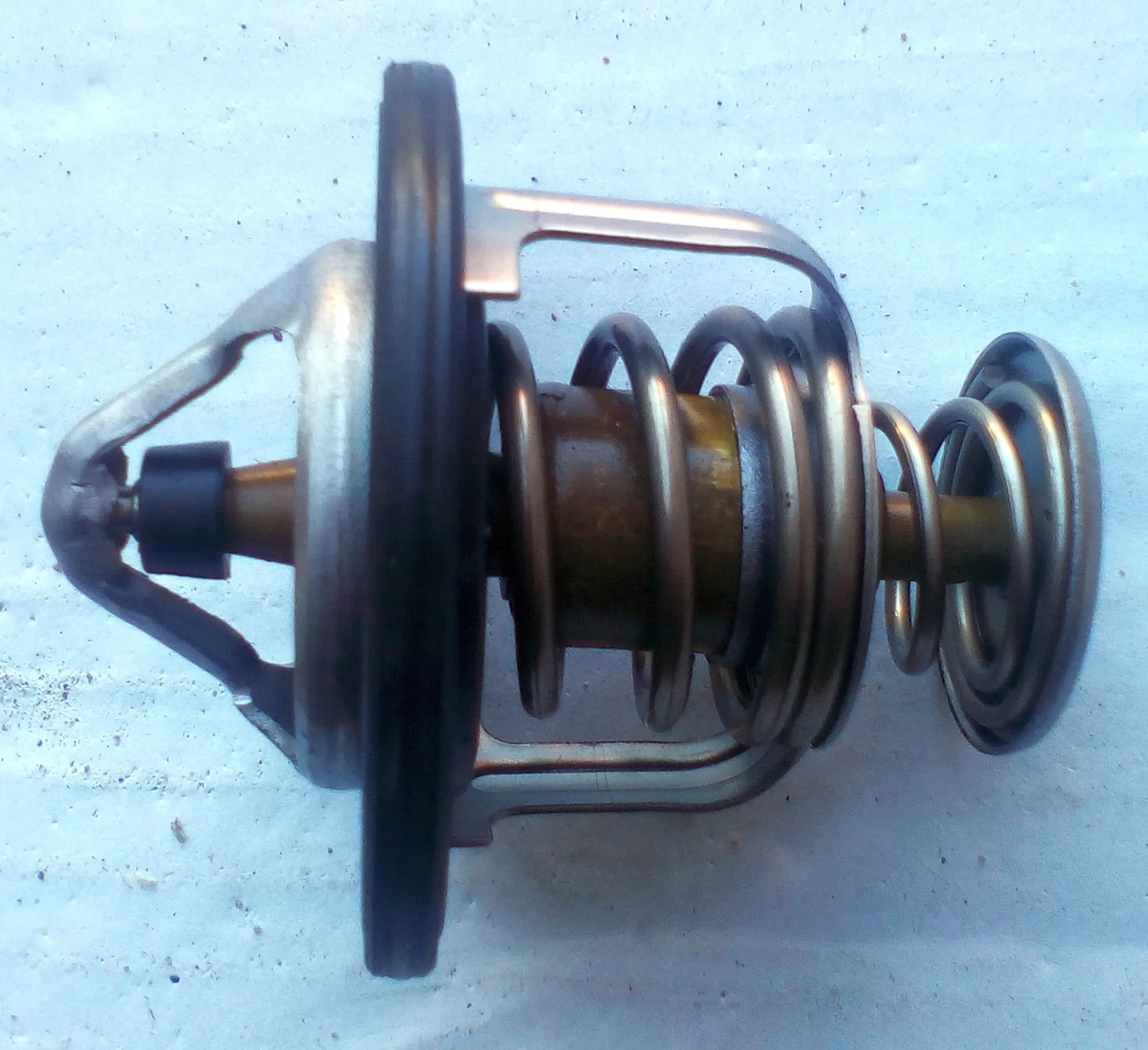 Automotive thermostat on its side, brass wax cup, coil spring, and rubber seal