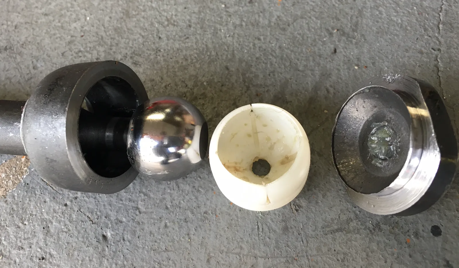 Inner tie rod cut open: steel ball, white plastic cup, and housing laid out on concrete