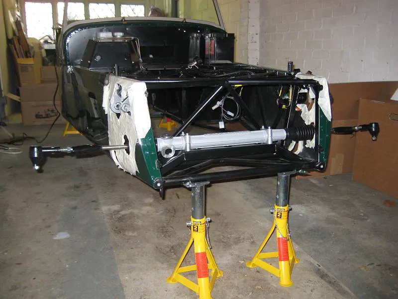 Caterham chassis on stands: silver steering rack spanning the front tubes, inner rods and outer ball-joint ends left and right