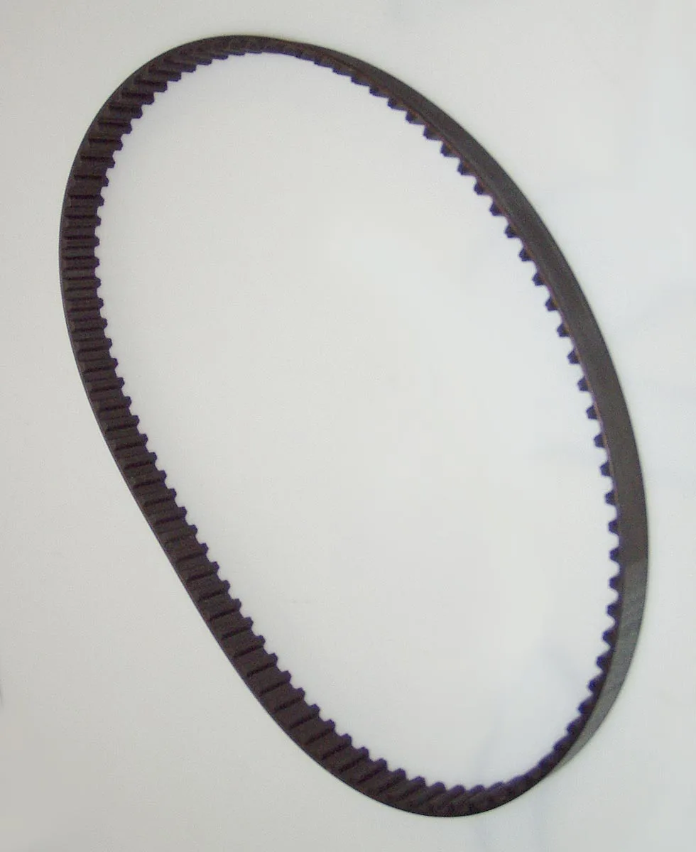 A black toothed belt lying in an oval on an off-white background. The teeth are on the inner face. The outer face is smooth. No markings are visible.