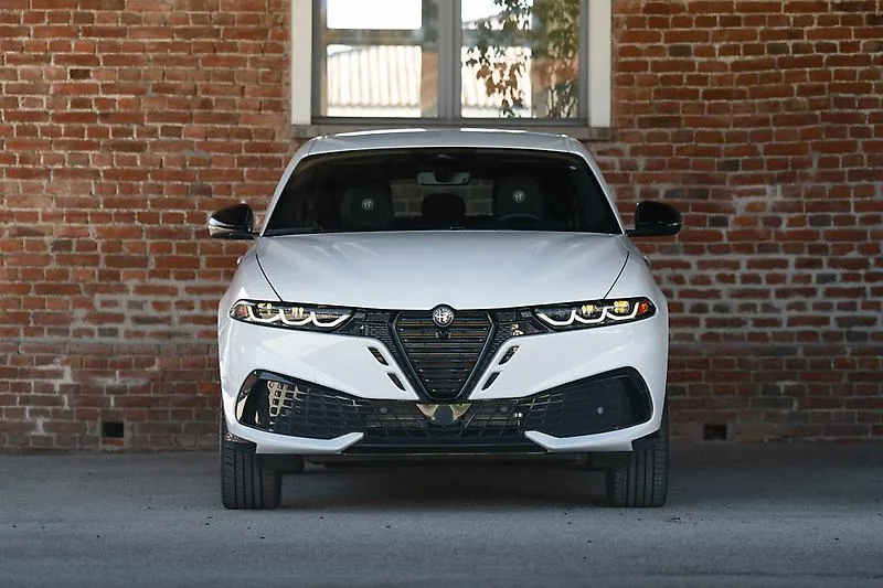 White 2026 Alfa Romeo Tonale Sport Speciale, dead-front against a brick wall with a concave scudetto, black-and-white badge, and trilobe lower intakes